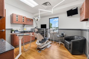 Fully equipped dental treatment room with chair, overhead equipment, and wooden cabinetry